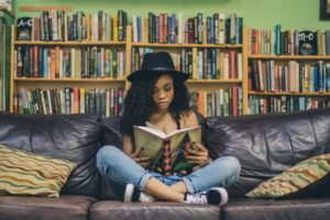 Image of young person sitting cross legged on a leather couch, reading a hardcover version of the novel "Water for Elephants"